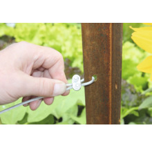 Hand bevestigt staalkabel met kabelklem aan een metalen paal in de tuin.