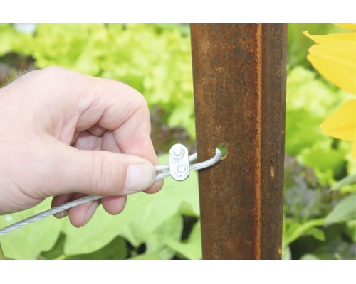 Hand bevestigt staalkabel met kabelklem aan een metalen paal in de tuin.
