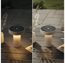 Een ronde solar tafellamp met een geribbelde voet staat op een houten tafel buiten, getoond bij daglicht en in de schemering.