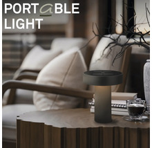 Draagbare LED tafellamp op een houten tafel in een gezellige woonkamer met fauteuils en decoratie.