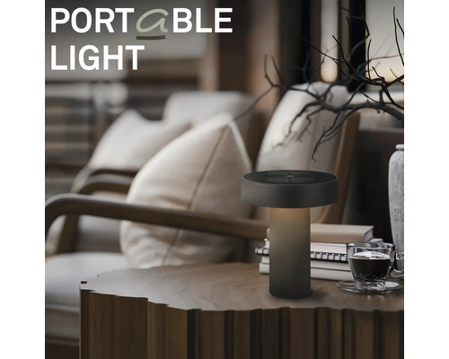 Draagbare LED tafellamp op een houten tafel in een gezellige woonkamer met fauteuils en decoratie.