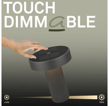 Een hand bedient de touch dimfunctie op een moderne LED tafellamp met een geribbelde voet en een platte lampkop.