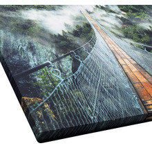 Close-up van een kunstafdruk met een hangbrug over een beboste canyon
