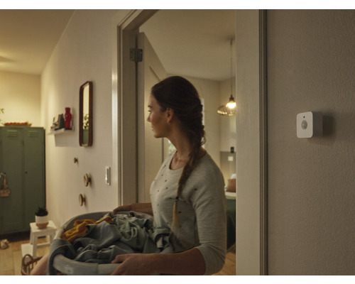 Vrouw met wasmand in hal met bewegingssensor aan de muur