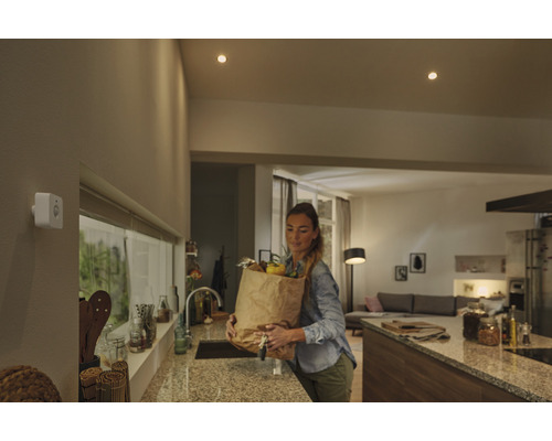 Vrouw met boodschappentas in de keuken onder plafondlampen en een bewegingssensor.