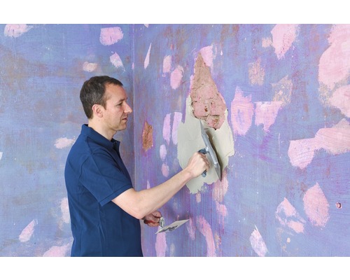 Een man plamuurt een gat in de muur met een plamuurmes.