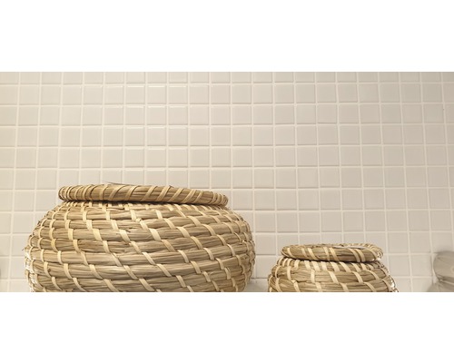 Twee gevlochten manden met deksel voor een muur met kleine vierkante tegels.