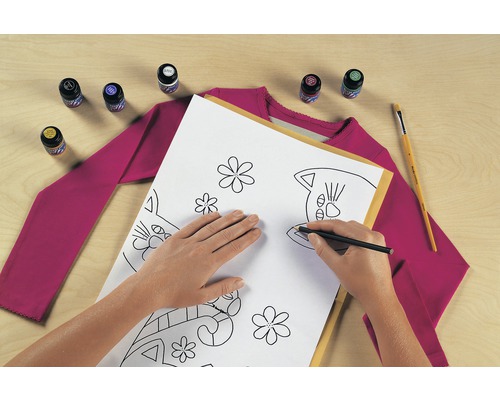 Scène met een persoon die met een pen een kattenpatroon op een vel papier tekent, samen met textielverf, een penseel en een T-shirt.