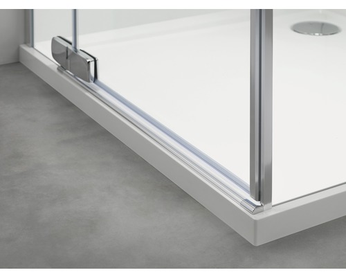 Detailopname van een douchecabine met glazen wand en metalen elementen op een douchebak.