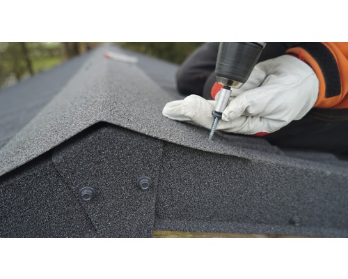 Een vakman bevestigt dakshingles met een accuschroevendraaier op een dak.