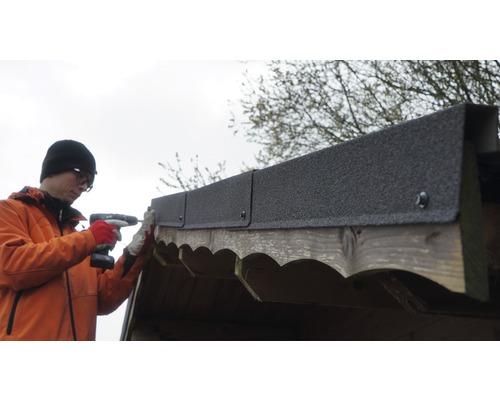 Man bevestigt dakleer met een accuschroevendraaier op een houten schuur.