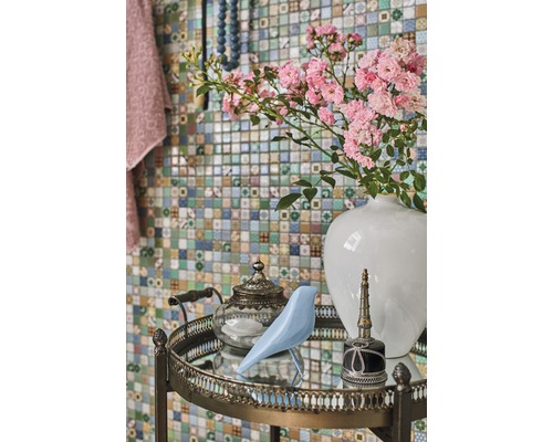 Decoratieve opstelling met bloemen, vogel, theepot en parfumflesje op een bijzettafel voor een mozaïekmuur