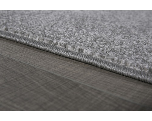 Detailopname van een grijs tapijt met festonrand op een houten vloer.