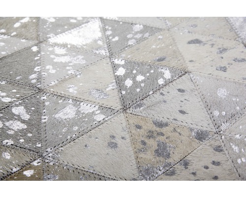 Close-up van een tapijt gemaakt van stukken leer met een geometrisch patroon en zilveren accenten.