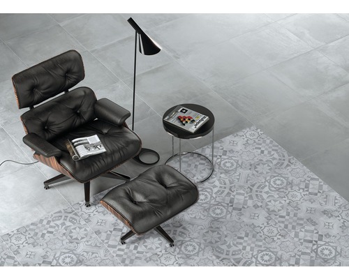 Lichte kamer met vloertegels in betonlook, gecombineerd met decoratieve tegels in grijze vintage stijl, fauteuil, lamp en bijzettafel