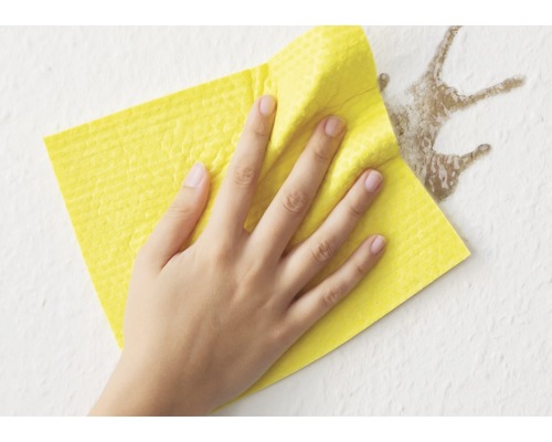 Een hand veegt een vlek van een muur met een gele reinigingsdoek.