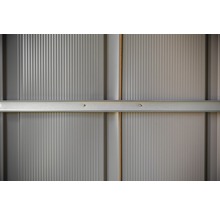 Detail van een grijze metalen wand met verticale ribbels en horizontale versteviging