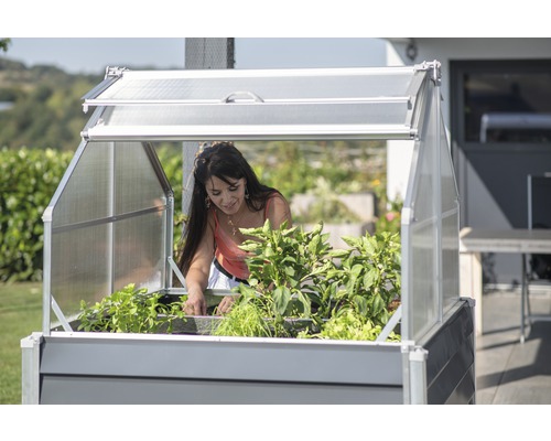 Vrouw tuiniert in een verhoogde tuinbak met broeikasopzetstuk in de tuin.