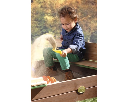 Een kind speelt met een gele vorm in een zandbak met zitbank.