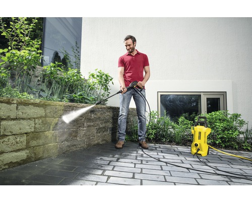 Een man reinigt een stenen muur met een Kärcher hogedrukreiniger buitenshuis.