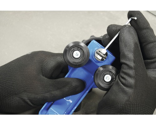 Close-up van handen met werkhandschoenen die een blauwe tegelsnijmachine afstellen met een inbussleutel.