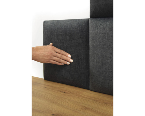 Persoon raakt grijs wandpaneel met textielbekleding aan op een houten vloer.