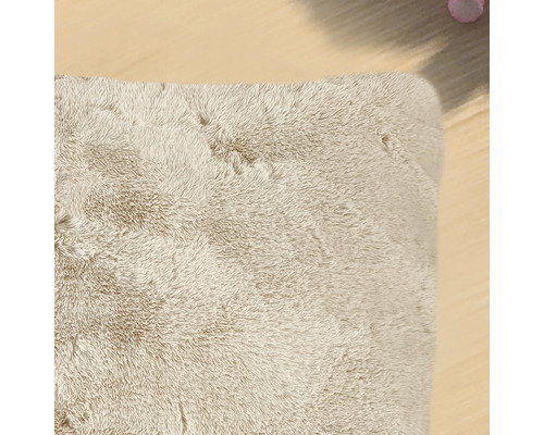 Detail van een beige, rechthoekig hoogpolig tapijt.