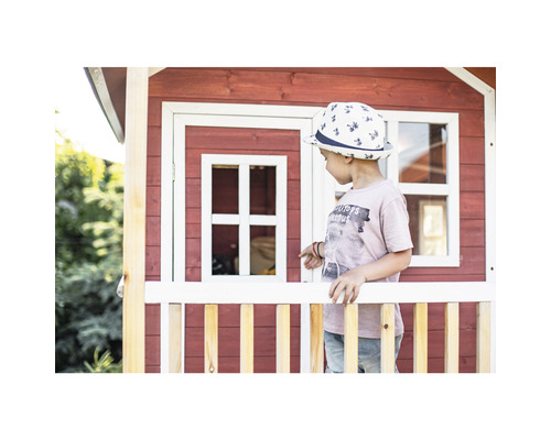 Kind staat voor een rood houten speelhuis met witte accenten
