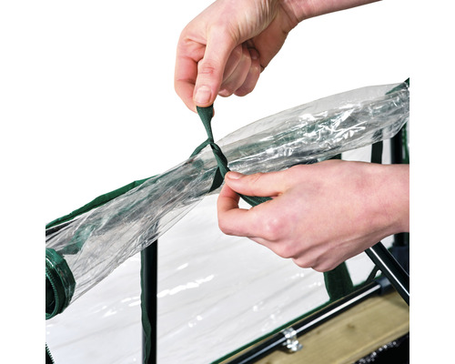 Iemand bevestigt een transparante folie met een groen lint aan een kweekbak.