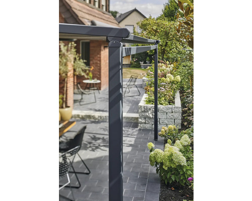 Detailopname van een terrasoverkapping in de tuin met bestrating en bloembed.