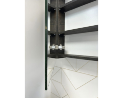 Detailopname van een spiegelkast met glazen plank en donkerhouten frame aan een witte muur met tegelpatroon