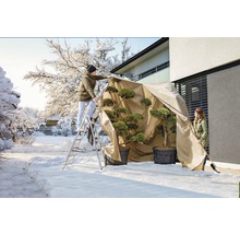 Personen beschermen planten met een winterbeschermhoes in de tuin