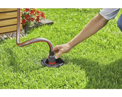 Iemand sluit een tuinslang aan op een wateraansluiting in de tuin