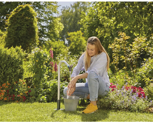 Een vrouw wast haar handen aan een tuinkraan met emmer in de tuin.
