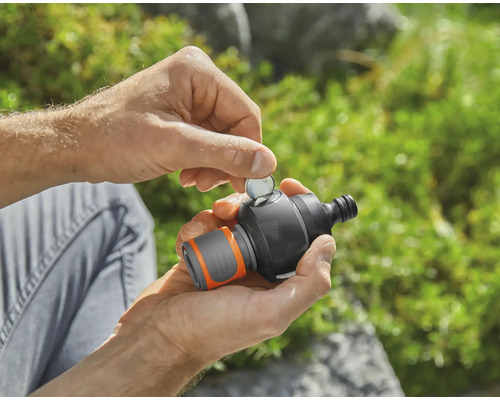 Een persoon steekt een munt in een tuinsproeier timer.