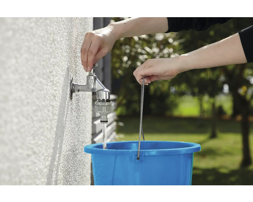 Een persoon vult een blauwe emmer met water uit een buitenkraan.