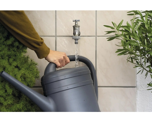 Persoon vult een gieter met water uit een kraan in de tuin