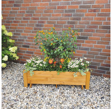 Houten plantenbak beplant met diverse bloemen voor een bakstenen muur