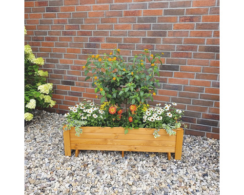 Houten plantenbak beplant met diverse bloemen voor een bakstenen muur