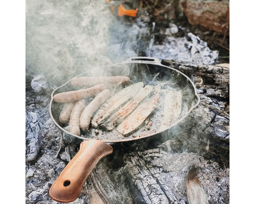 Braadworst en courgette in een gietijzeren pan boven een open vuur