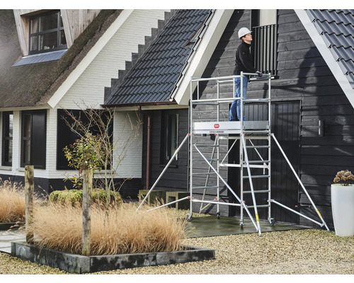 Een persoon op een rolsteiger voor een huis.