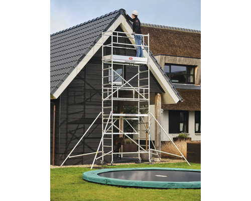 Een persoon gebruikt een aluminium rolsteiger voor werkzaamheden aan een huis.