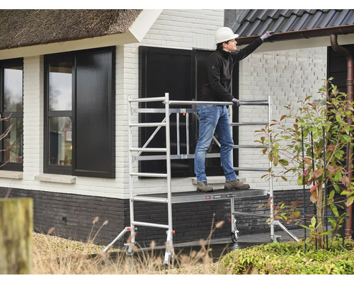 Een persoon staat op een steiger en werkt aan een huis.