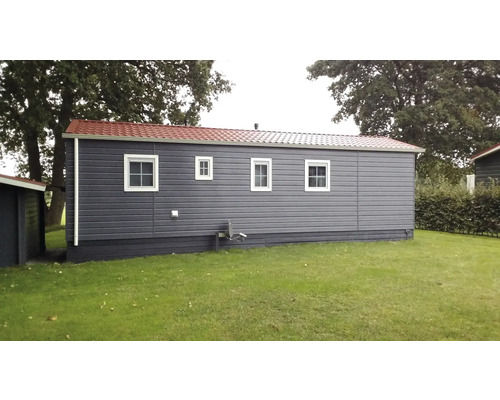 Grijs stacaravan met drie ramen en een rood dak op een gazon.