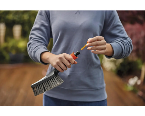 Een persoon bevestigt een gele sproeikop aan een borstel voor tuinreiniging.