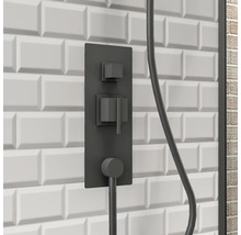 Zwarte douchearmatuur op een witte wand met rechthoekige tegels