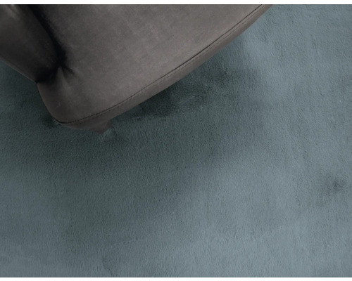 Detailopname van een hoogpolig tapijt met een deel van een zitmeubel.