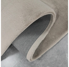 Detailweergave van een beige tapijt met gekrulde hoek, dat de textuur en onderkant laat zien