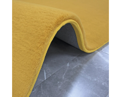 Detailweergave van een goudgele vloerkleed met een textielen rug