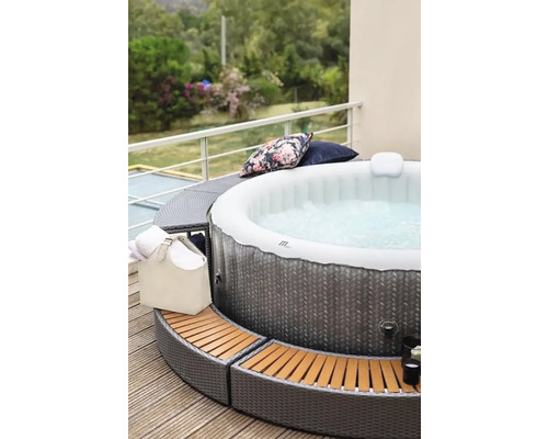 Opblaasbare jacuzzi met rotan omranding op een terras met kussens en handdoeken